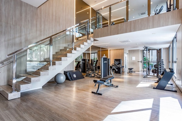 Un gimnasio de varios niveles con una escalera, equipo de ejercicio y un ventanal grande.
