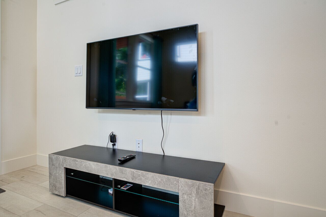 Un salon moderne avec un téléviseur à écran plat fixé au mur, un meuble de rangement de couleur sombre en dessous et une prise électrique sur le mur.