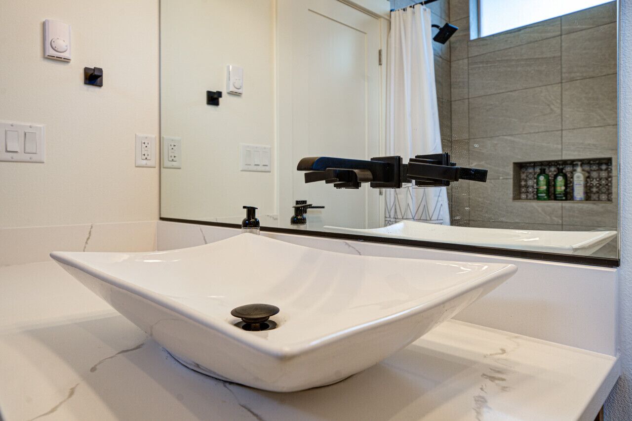 A bathroom with a white vessel sink, a large mirror, and a shower area.