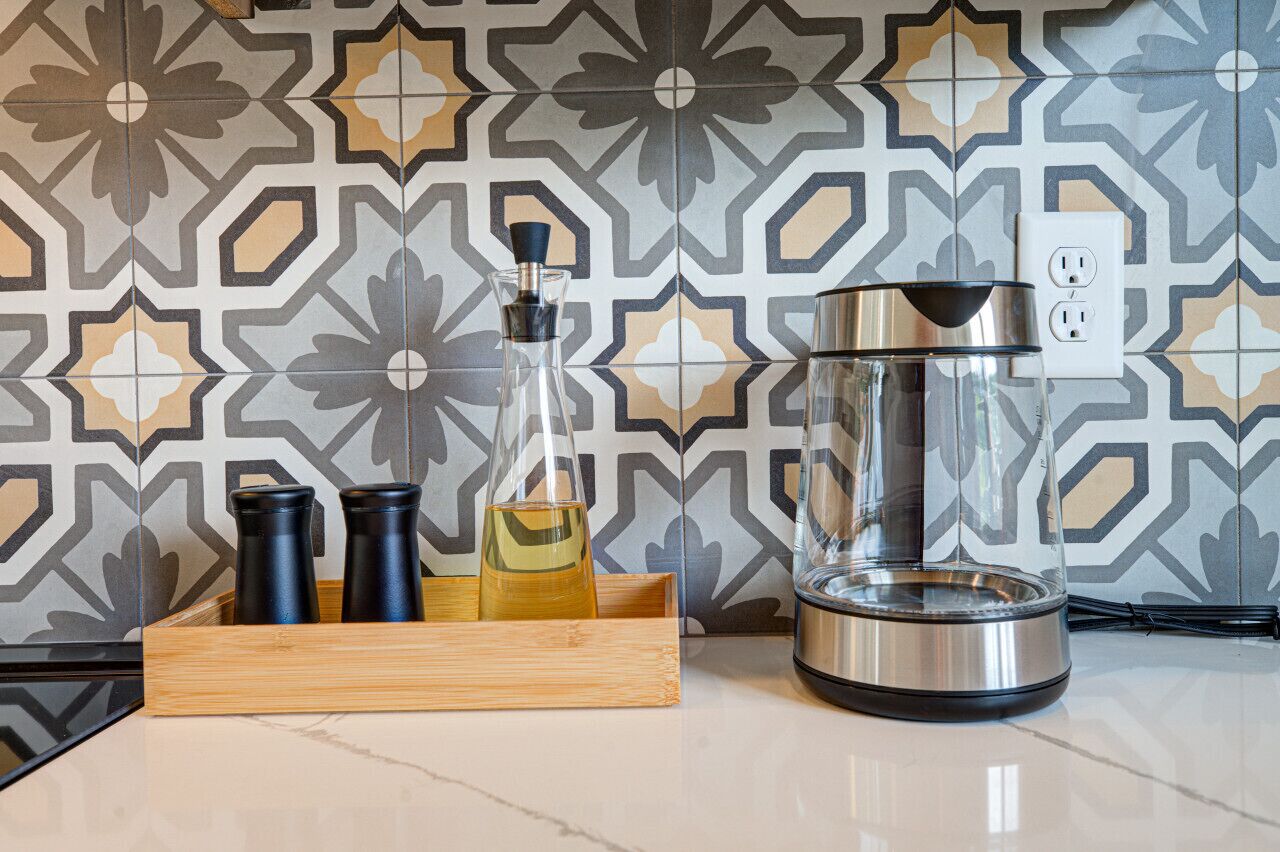 A kitchen with a coffee maker, a glass container, and two black containers on a wooden tray.