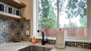 A kitchen with a stainless steel sink, a black faucet, and a window with a view of trees and a wooden fence. - Urban-chic Studio Guesthouse in a quiet neighborhood - near Intel and Nike (Hillsboro)