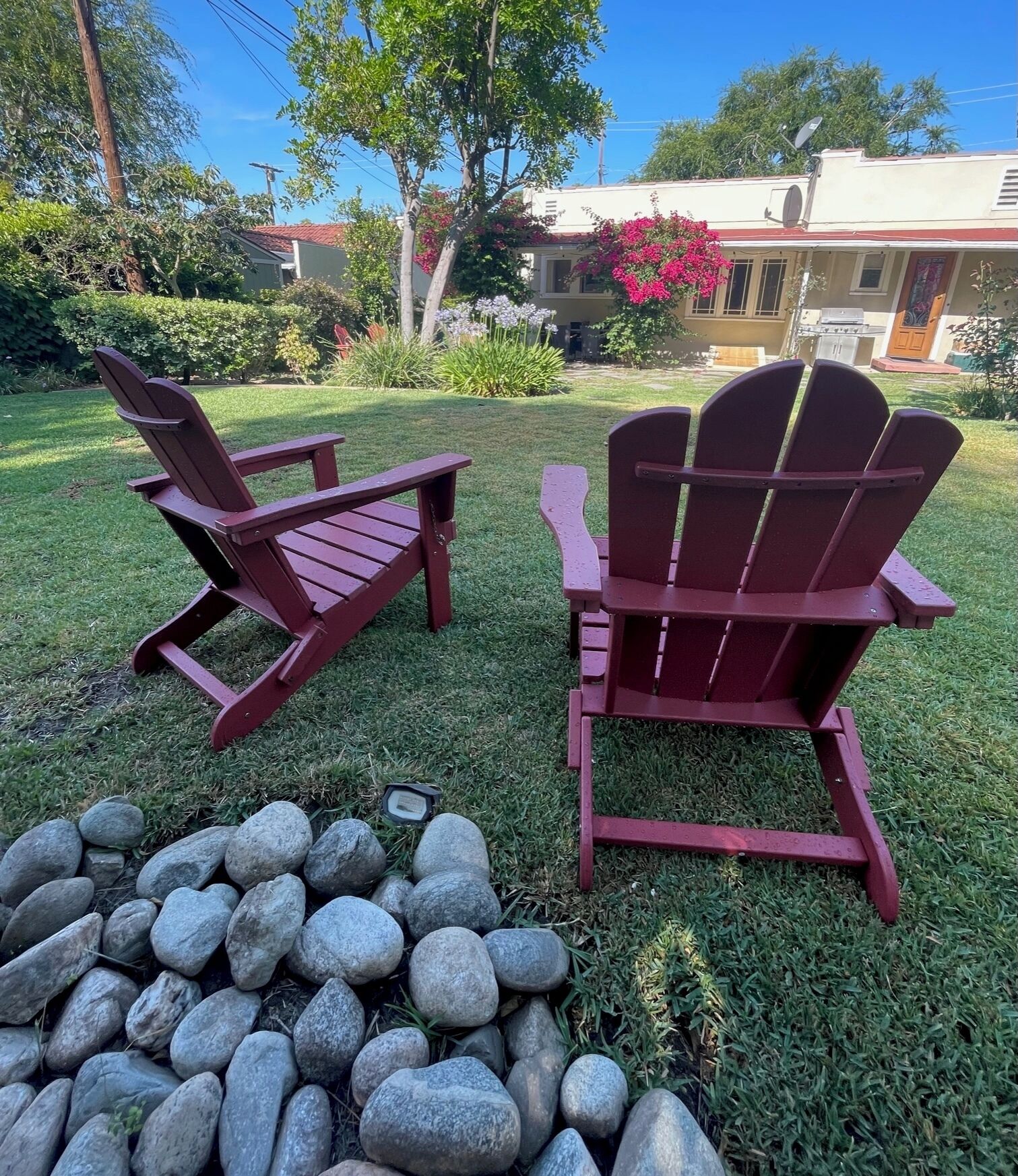Two Adirondack chairs in a grassy yard with a stone fire pit.