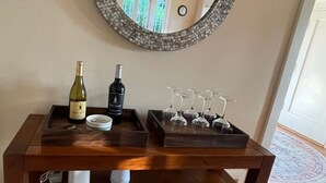 Een houten console tafel met daarboven een mozaïekspiegel, een wijnfles, glazen en een dienblad.