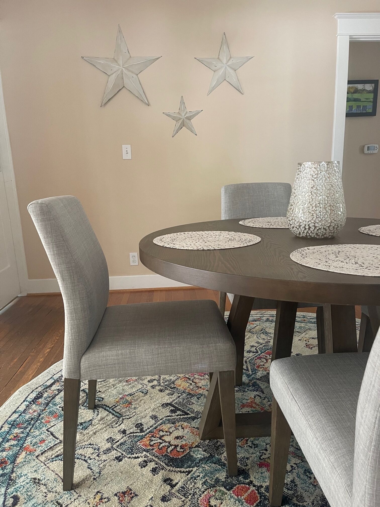 Un coin repas avec une table ronde, des chaises à revêtement gris, un tapis à motifs et des décorations murales en forme d’étoiles.