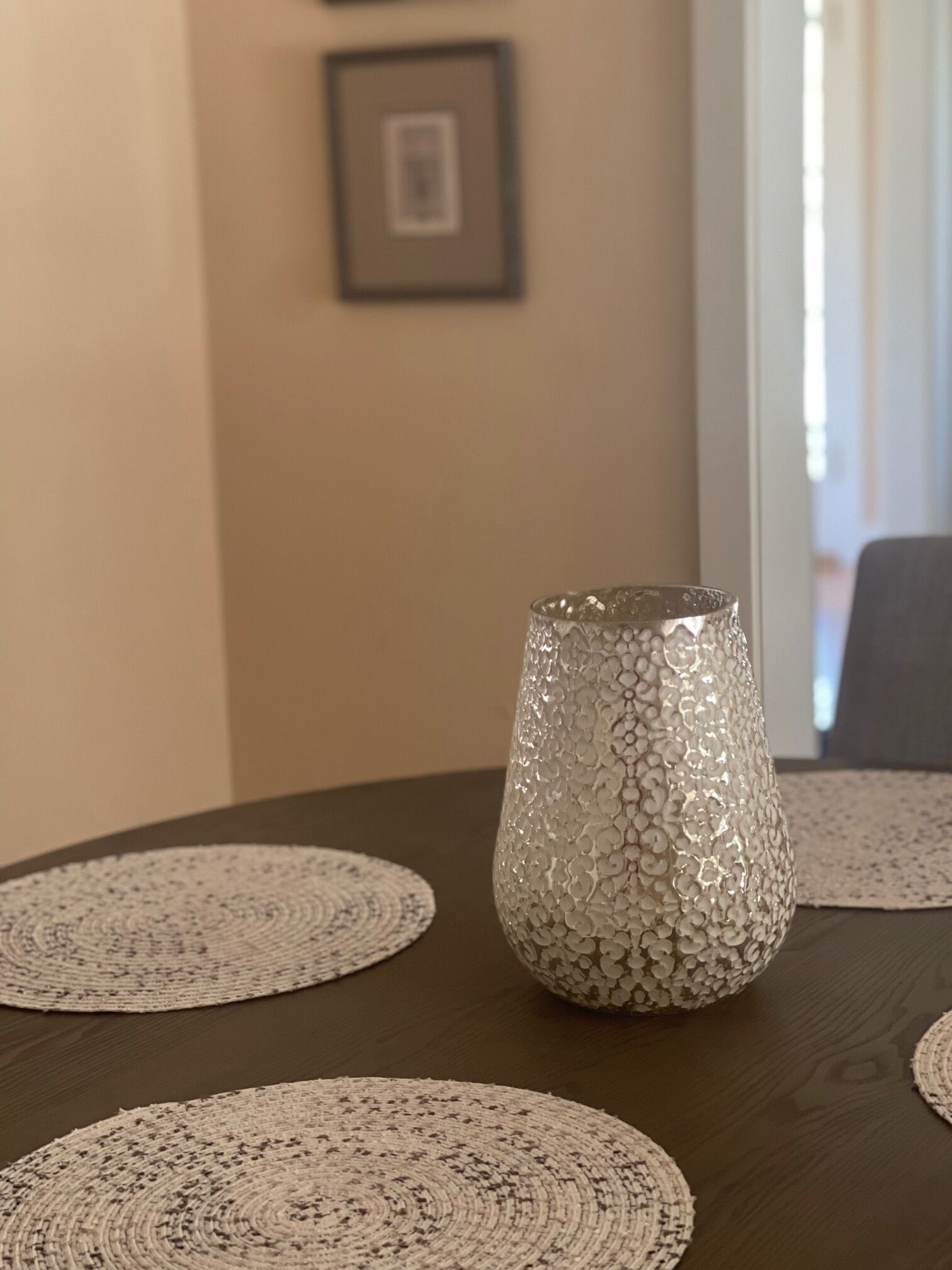 Una mesa de comedor con un florero de vidrio decorativo y individuales tejidos.