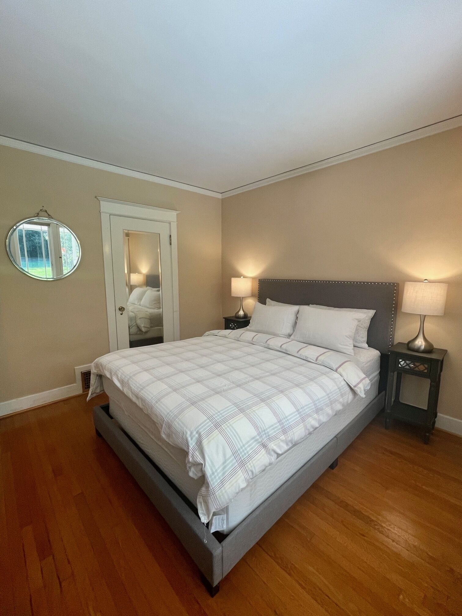 Une chambre à coucher avec un lit, deux tables de chevet, un miroir rond et une porte.