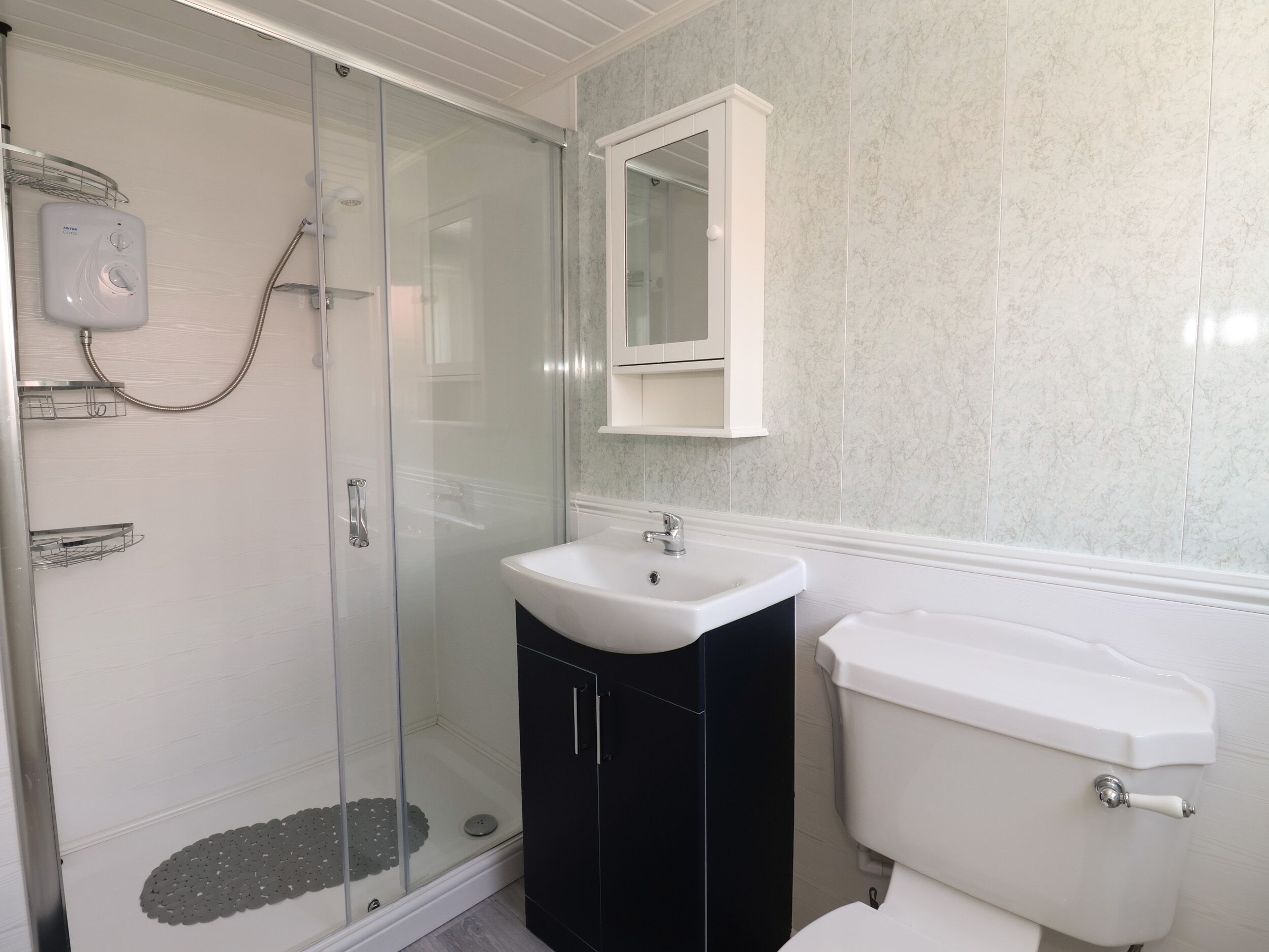 Un baño con cabina de ducha de vidrio, lavamanos blanco, mueble negro y retrete blanco.