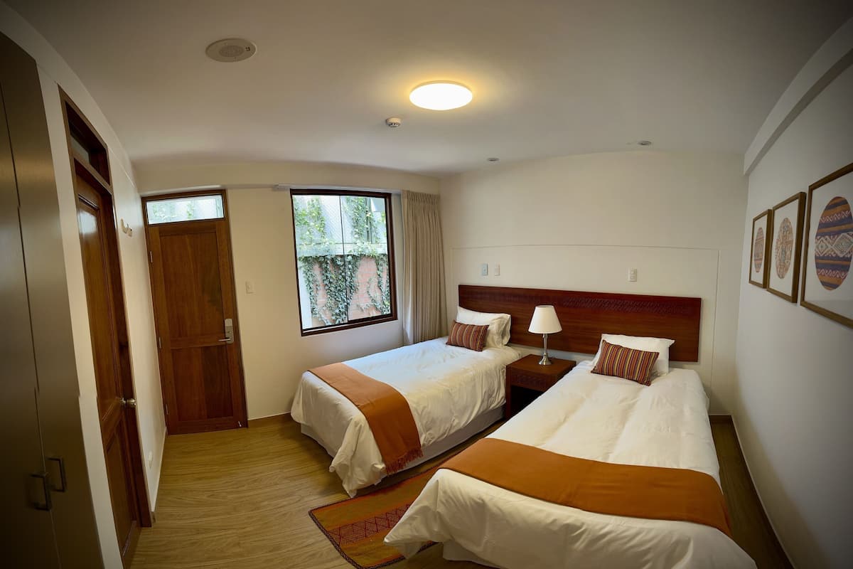 Habitación de hotel con dos camas, una ventana con vistas, un armario de madera y una lámpara en el techo.