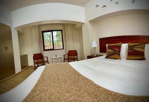 A hotel room with a large bed, a wooden headboard, a desk, a chair, a small table, and a window with curtains. - Inkantari Boutique Hotel (Cusco)