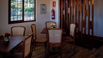 Un comedor con mesa y sillas de madera, una ventana con vista a follaje, un extintor y un panel divisor de madera.