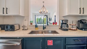 A kitchen with white cabinets, a stainless steel sink, a chandelier, and a coffee maker.