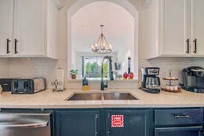 A kitchen with white cabinets, a stainless steel sink, a chandelier, and a coffee maker.