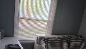 Een slaapkamer met een bed, een nachtkastje met handdoeken, een nachtkastje en een raam met jaloezieën.