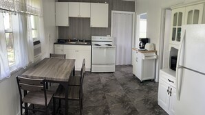 Een compacte keuken met witte kastjes, een fornuis, een koelkast en een eettafel met stoelen.