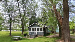 Een kleine hut met een veranda, omringd door bomen en een picknicktafel.