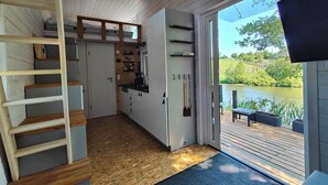 A compact kitchen with a view of a lake, a wooden staircase, and a deck. - Tiny House by a swimming pond with terrace & fireplace – Last Minute (Großharthau)