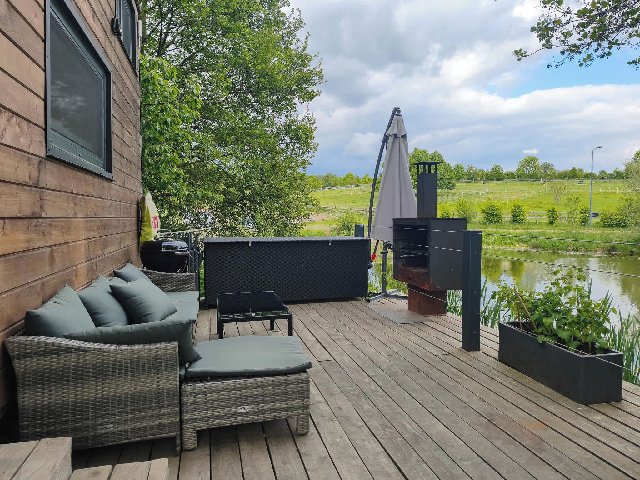 A wooden deck with outdoor furniture, a grill, and a view of a pond and field.
