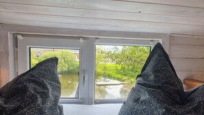 A room with a bed, two bean bags, and a window with a view of a pond and greenery. - Tiny House by a swimming pond with terrace & fireplace – Last Minute (Großharthau)