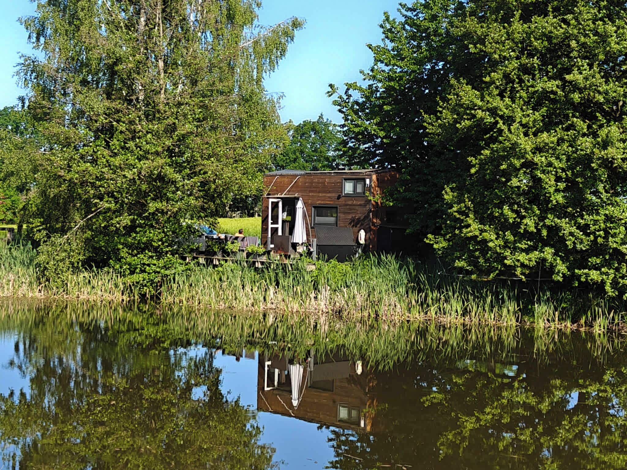 A house with a small deck and a door, surrounded by trees and a body of water.