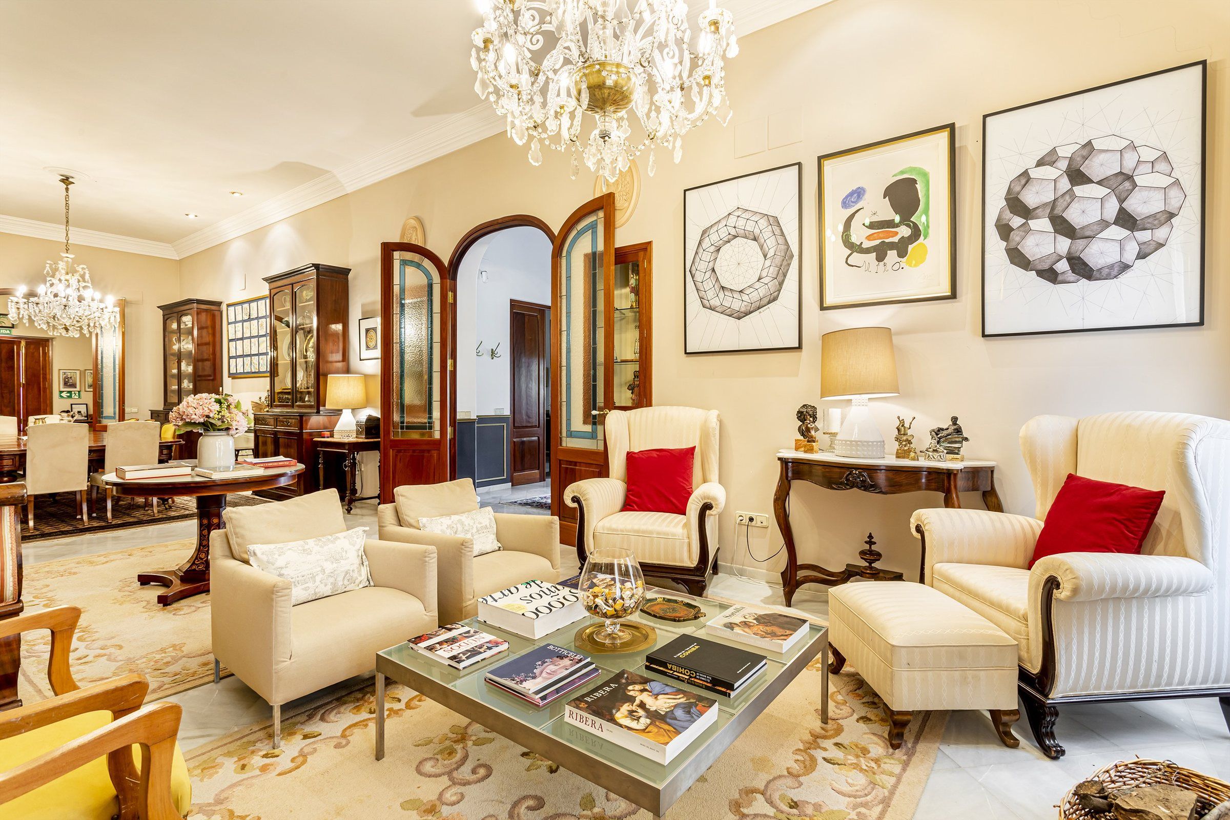 Un salon spacieux agrémenté d’un lustre, de fauteuils, d’une table basse avec des livres et d’œuvres d’art encadrées accrochées aux murs.