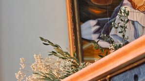 Una obra de arte enmarco que muestra a una mujer con vestimenta tradicional, una cesta tejida y un jarrón con flores.