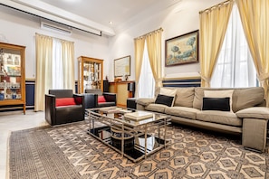 Una sala de estar con un sofá, sillones, una mesa de centro, un aparador con cristalería y un cuadro en la pared.