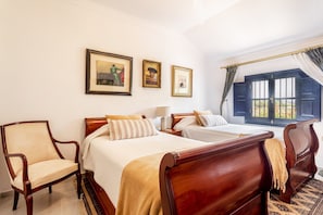 A hotel room with two beds, a chair, a nightstand, and a window with curtains.