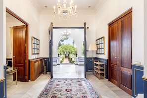 A hallway with a chandelier, wooden doors, and a view of a garden.