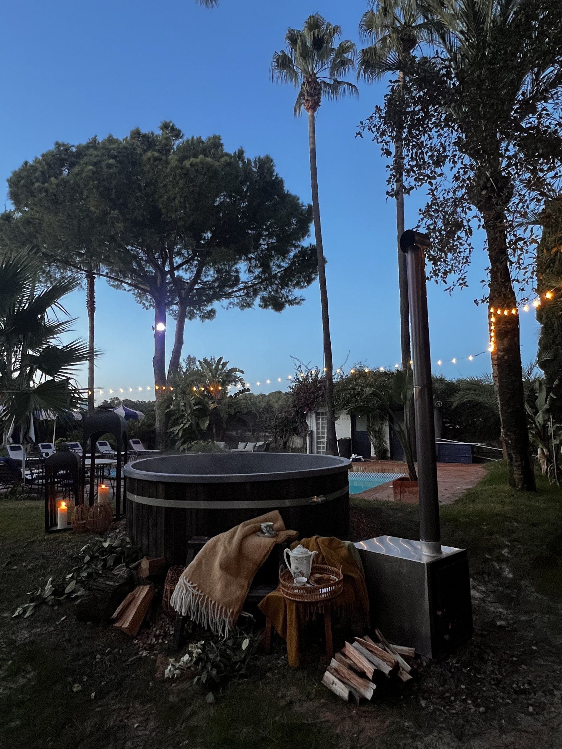 Un área de estar al aire libre con jacuzzi, sillones reclinables y luces colgantes.
