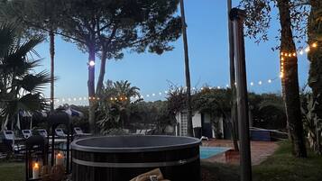 Un área de estar al aire libre con jacuzzi, sillones reclinables y luces colgantes.