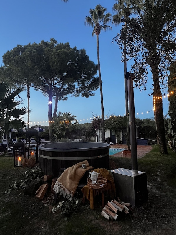 An outdoor seating area with a hot tub, lounge chairs, and string lights.