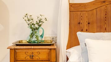 Une table de chevet en bois avec des tiroirs, un vase en verre avec des fleurs, une table de chevet, un lit avec une literie blanche et une tête de lit en bois.