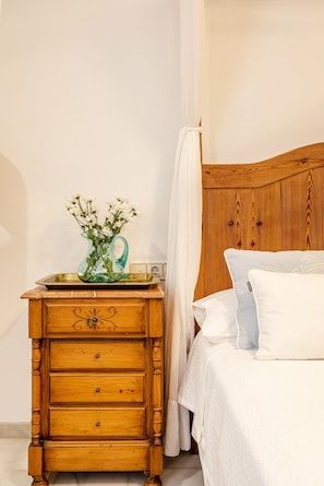 A wooden nightstand with drawers, a glass vase with flowers, a bedside table, a bed with white bedding, and a wooden headboard. - 16th-century villa for 14, near Valencia | Villa Paula (Manises)