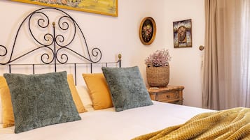 Un lit bien fait, avec une tête de lit, deux oreillers, une couverture et une petite table de chevet sur laquelle se trouve un panier de fleurs.