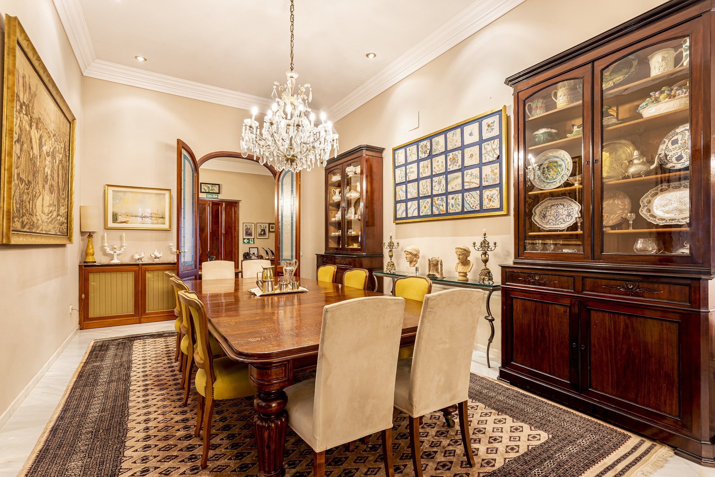 Een stijlvolle eetzaal met een houten tafel, stoelen, een kroonluchter en een vitrinekast.