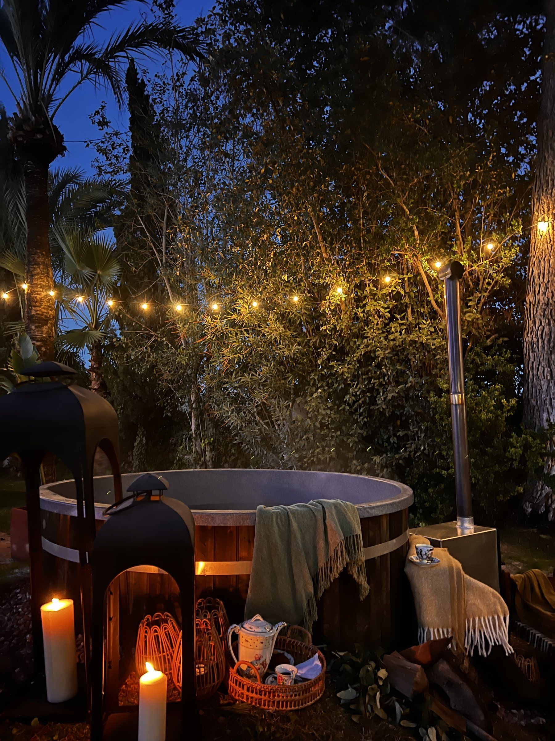 Un bain à remous entouré d’arbres, illuminé de guirlandes lumineuses et agrémenté de bougies.