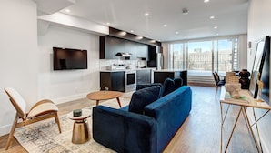 Una sala de estar moderna con un sofá azul, una silla de madera, una mesita redonda y un televisor de pantalla plana montado en la pared.
