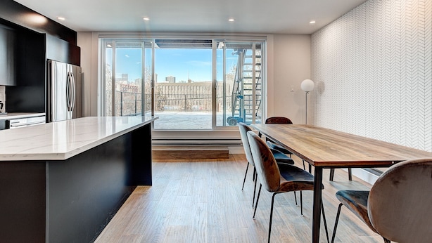 Una cocina moderna con una isla grande, un comedor con una mesa y sillas de madera, y vistas de la ciudad a través de amplias ventanas.