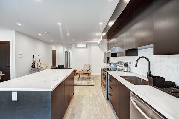 A modern kitchen with a large island, dark cabinetry, and white countertops. - Burgundy Lofts - Marché Atwater (Montreal)