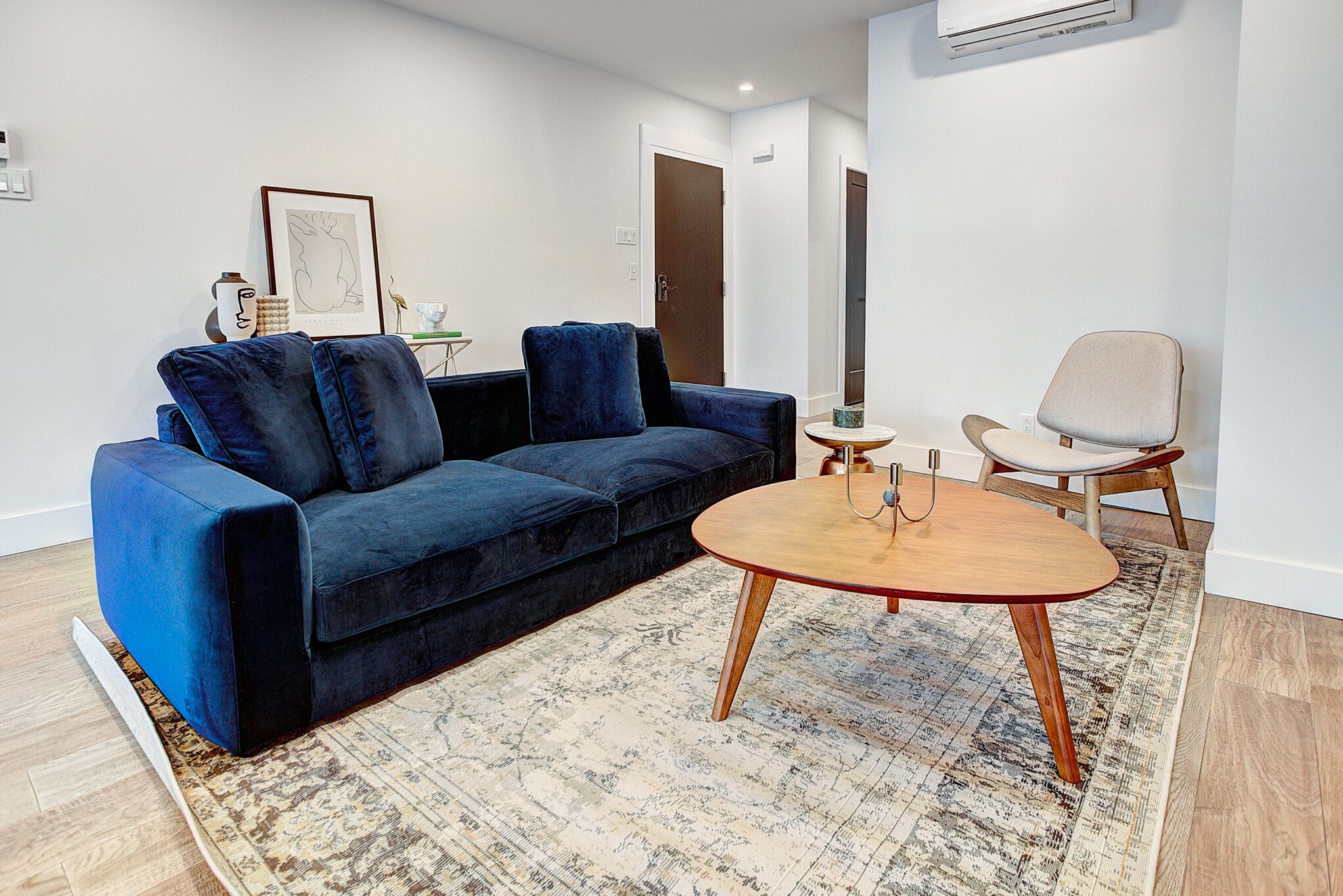 A modern living room with a dark blue sofa, a round wooden coffee table, and a light-colored armchair.