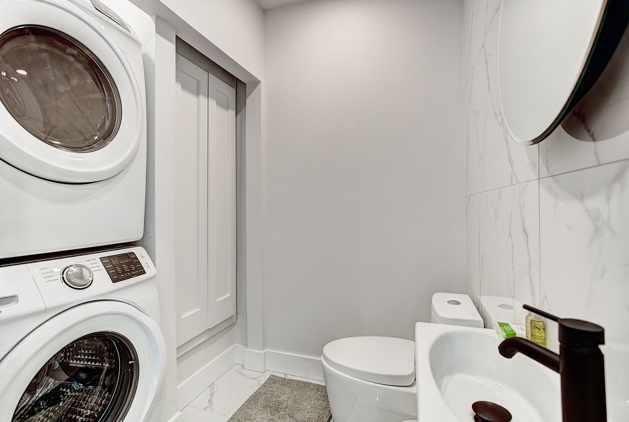 A compact bathroom with a washing machine, toilet, and sink.