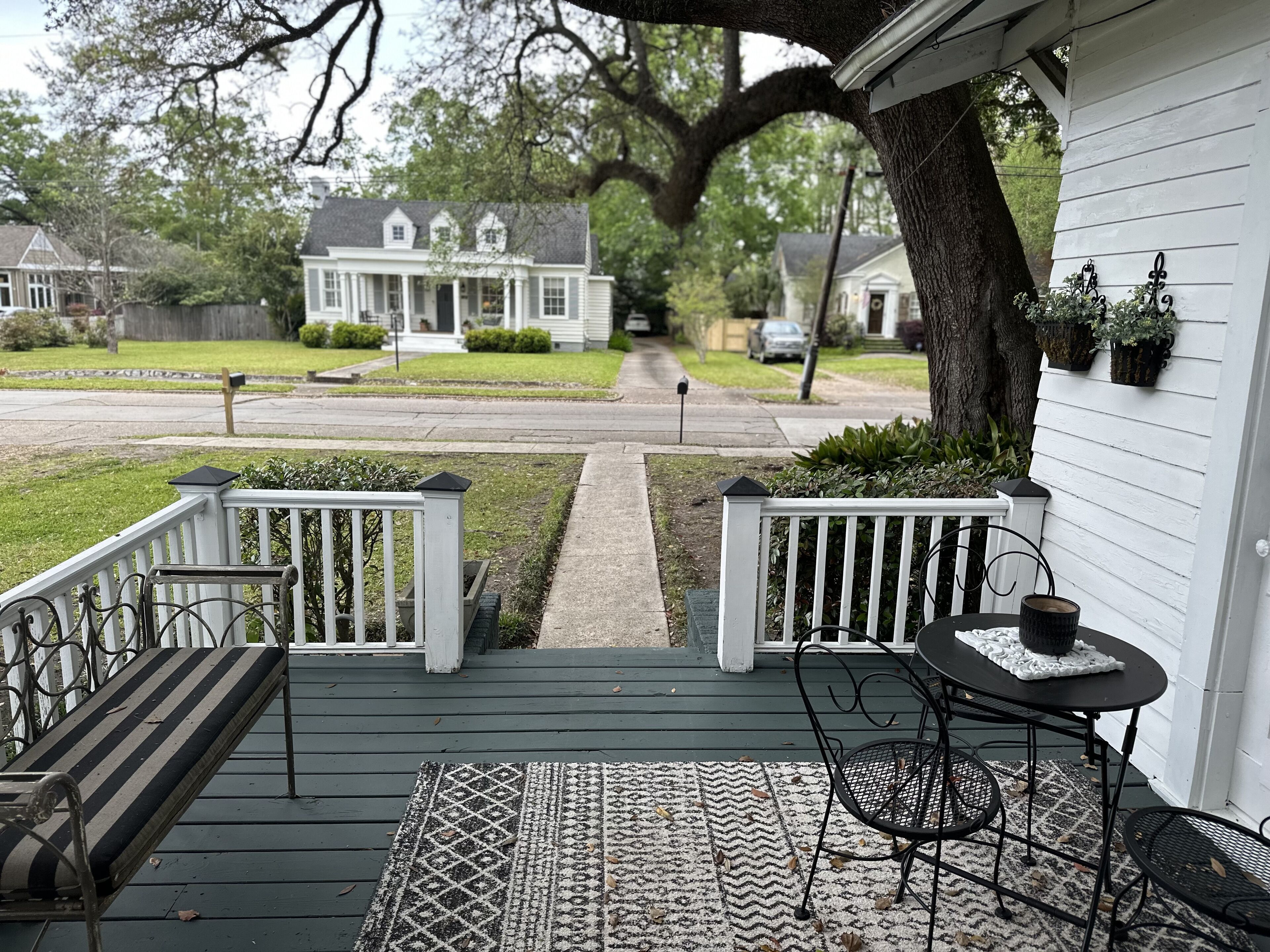 Eine Veranda mit einer Bank und einem Tisch, ein Baum und Blick auf eine Straße mit Häusern.