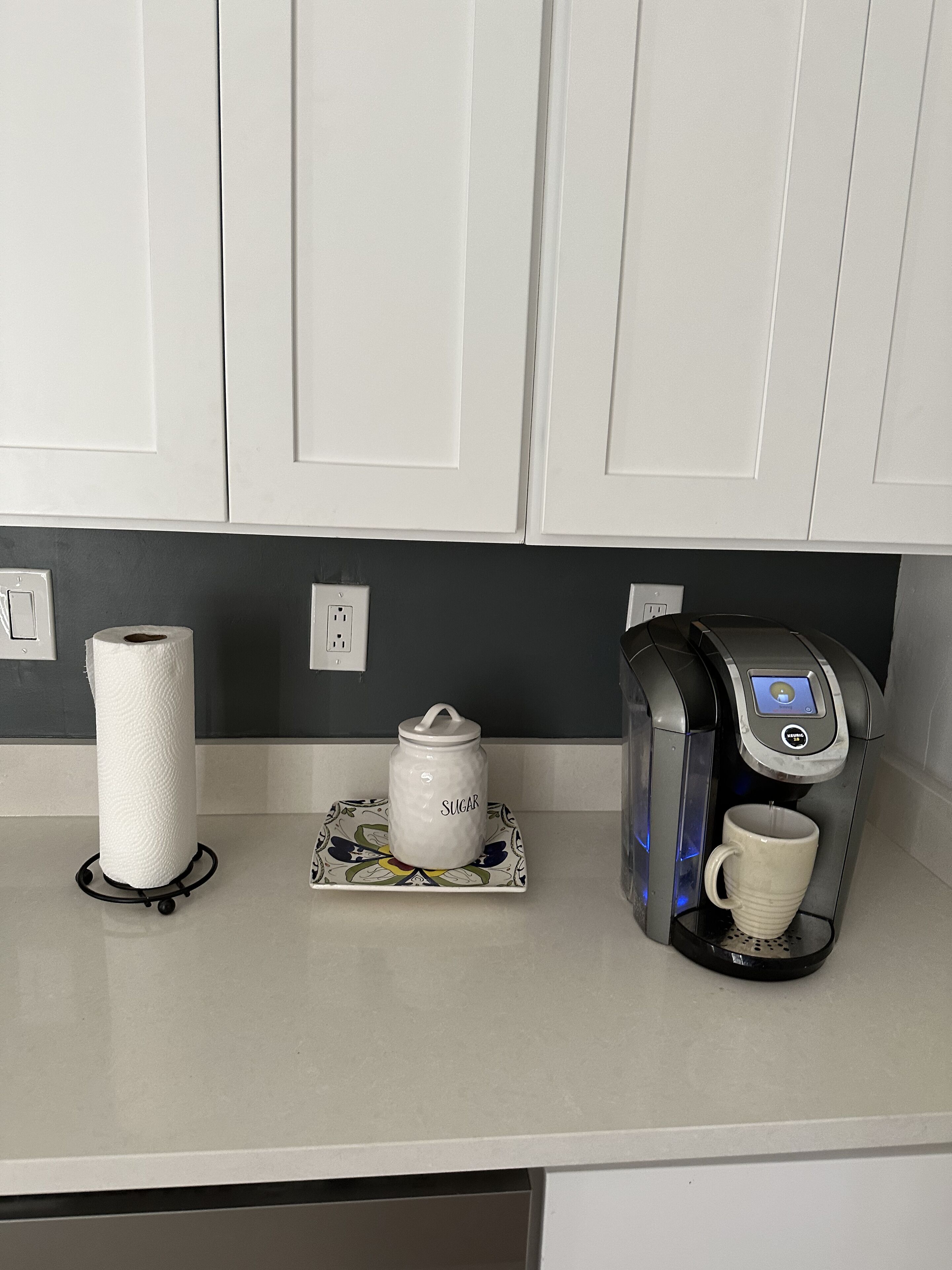 A kitchen counter with a paper towel holder, a sugar jar, and a coffee machine.