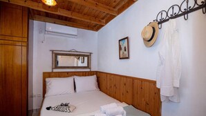 Une chambre à coucher avec une tête de lit en bois, un lit recouvert de draps blancs, un miroir au-dessus du lit, un chapeau et un manteau suspendus à un porte-manteau.