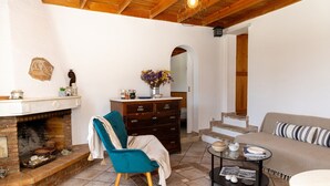 Uma sala de estar aconchegante com lareira, uma poltrona azul-turquesa, um aparador de madeira e um sofá com almofadas listradas.
