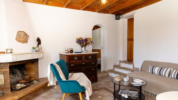 Un salon chaleureux avec une cheminée, un fauteuil turquoise, une commode en bois et un canapé agrémenté de coussins à rayures.