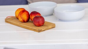Une planche à découper en bois avec des pêches, posée sur une table blanche.