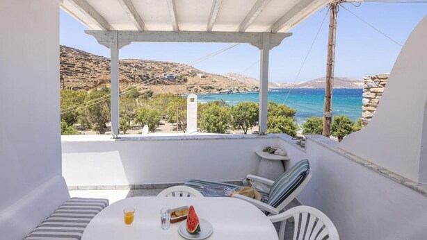 Uma varanda com mesa, cadeiras e vista para o mar e as colinas.