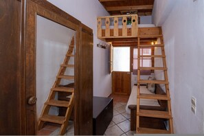 A room with a wooden ladder leading to a loft bed, a wooden door, and a small window. - Anemelo Beach House in Panormos (Tinos)