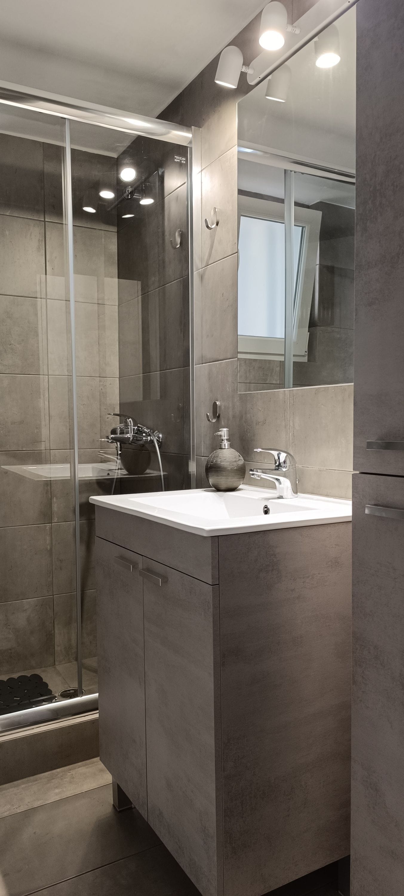 A modern bathroom with a glass shower enclosure, a white sink, and a large mirror.